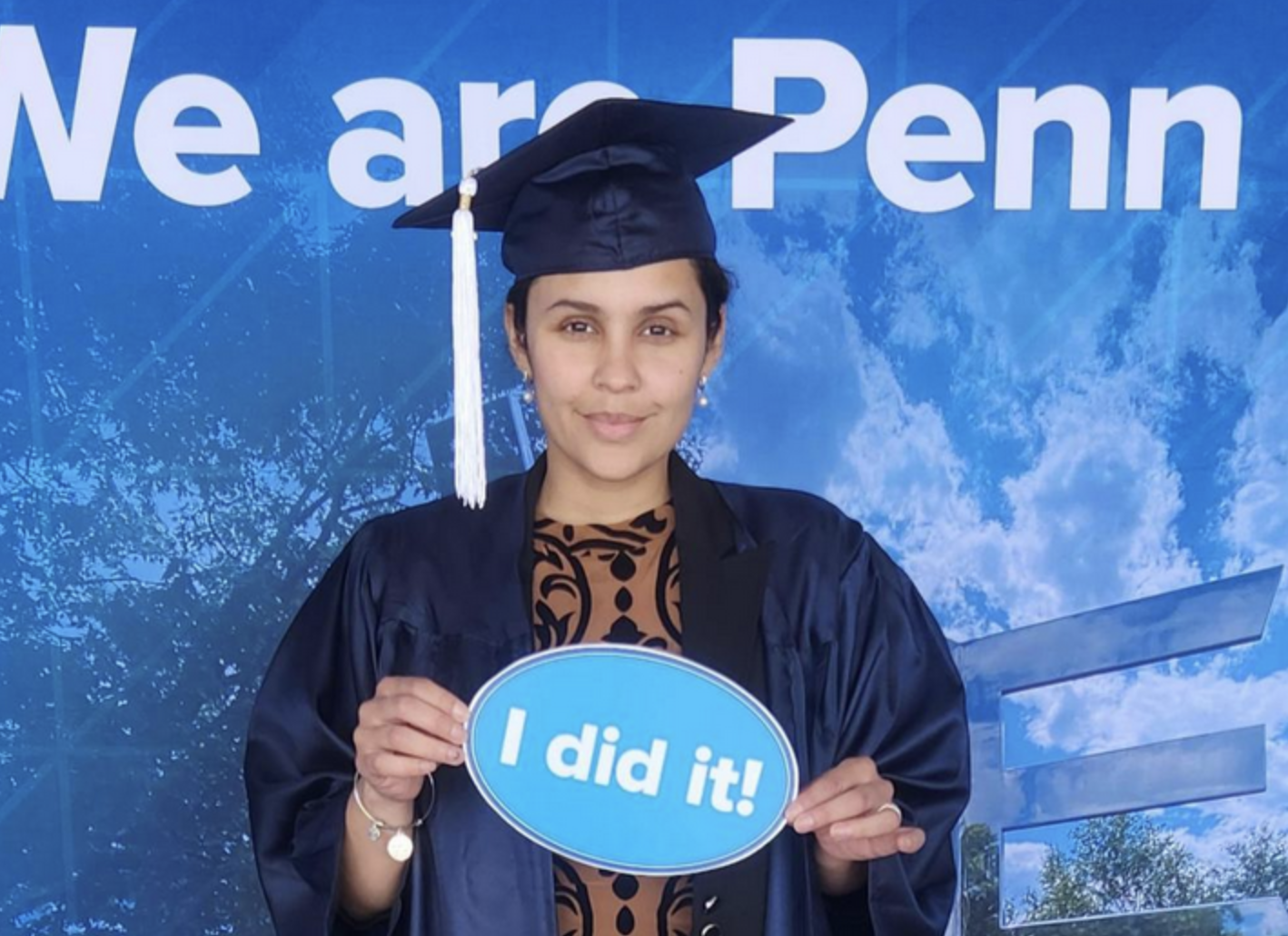 graduate in a cap and gown holding a sign that reads 'I did it!'