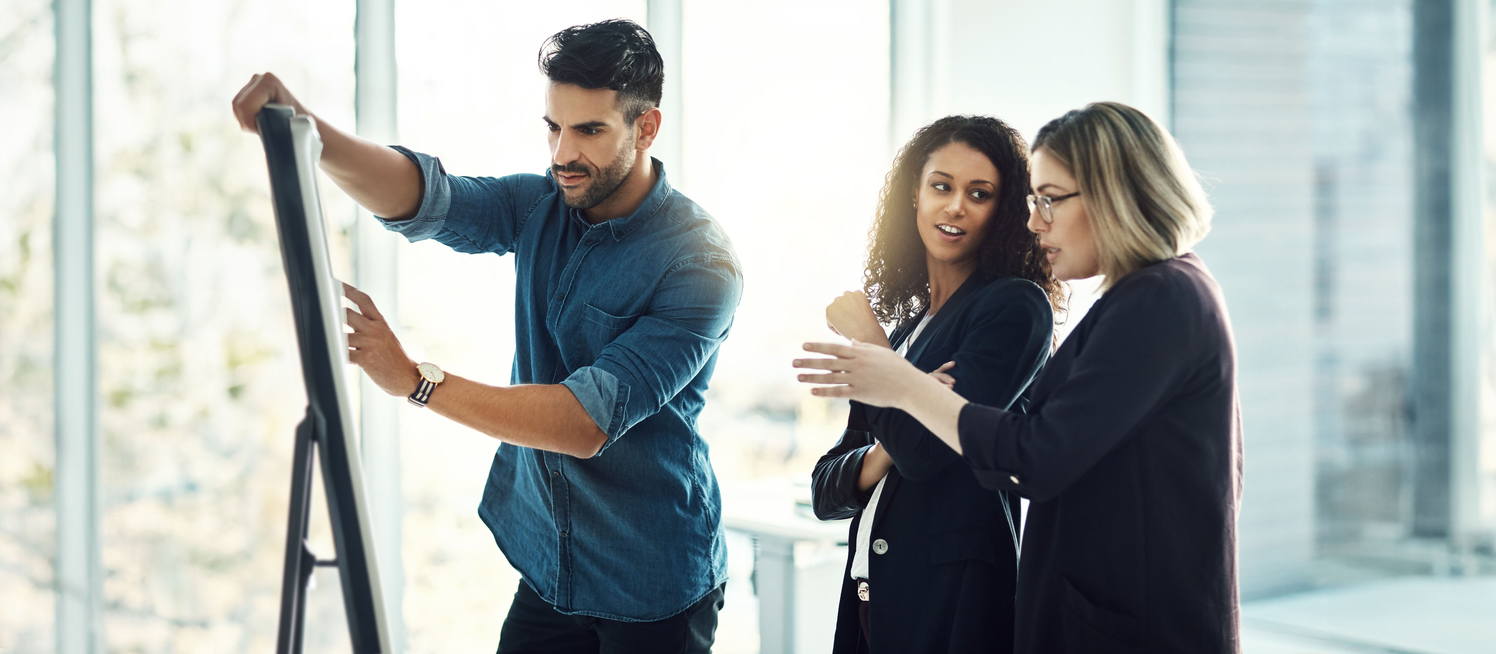 Two women discuss as their male coworker writes on a whiteboard.