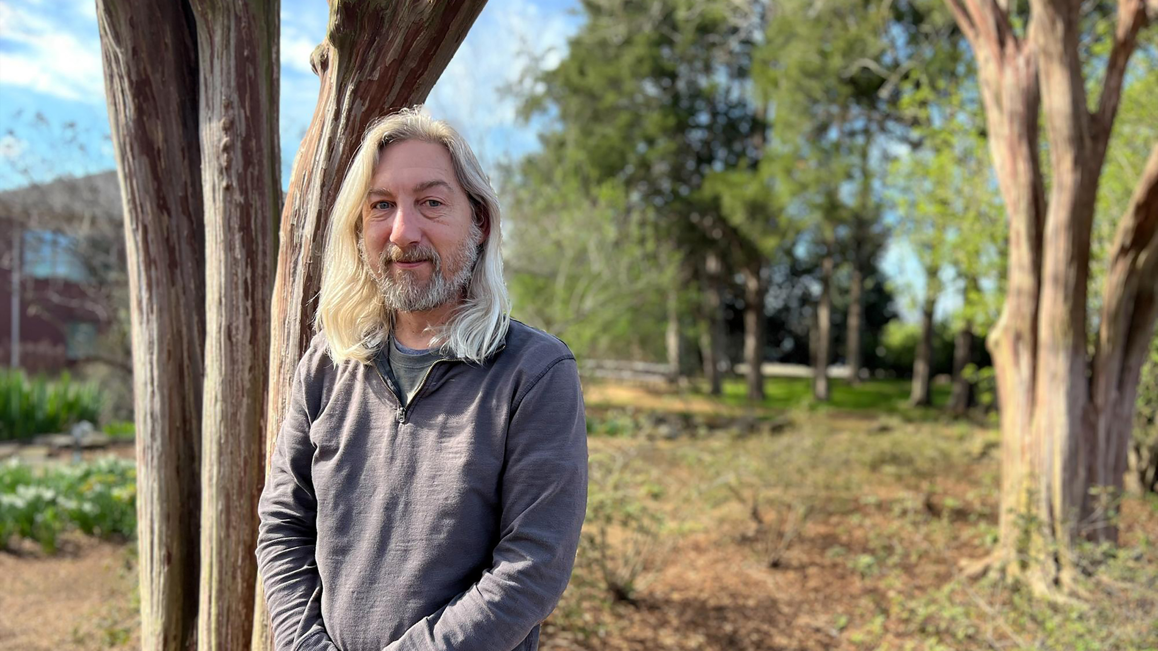 A man standing in a landscaped area with trees.