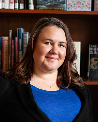 A woman poses in front of a bookshelf for a headshot.