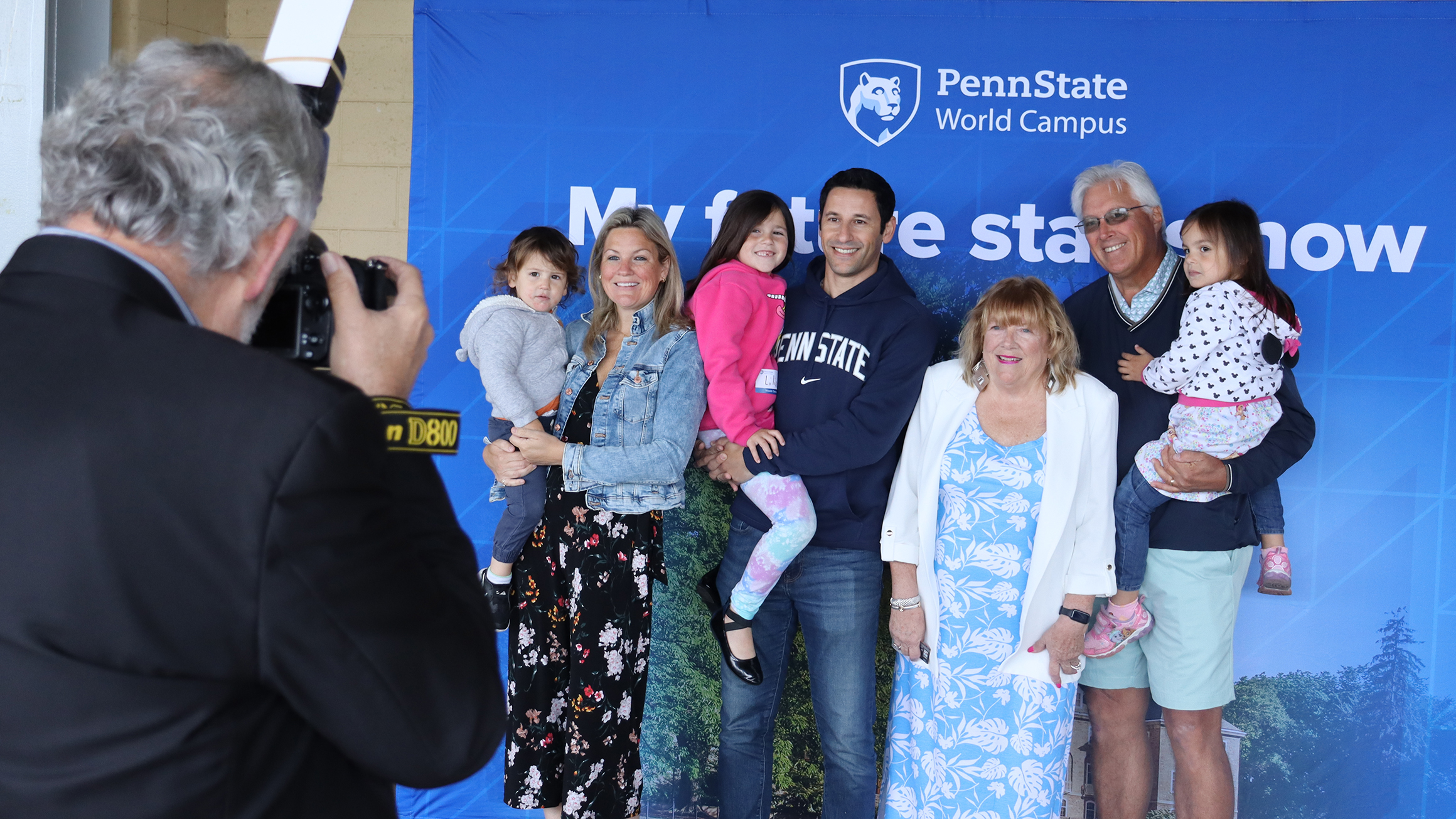 A man takes a photo of a group of people in front of a blue background.