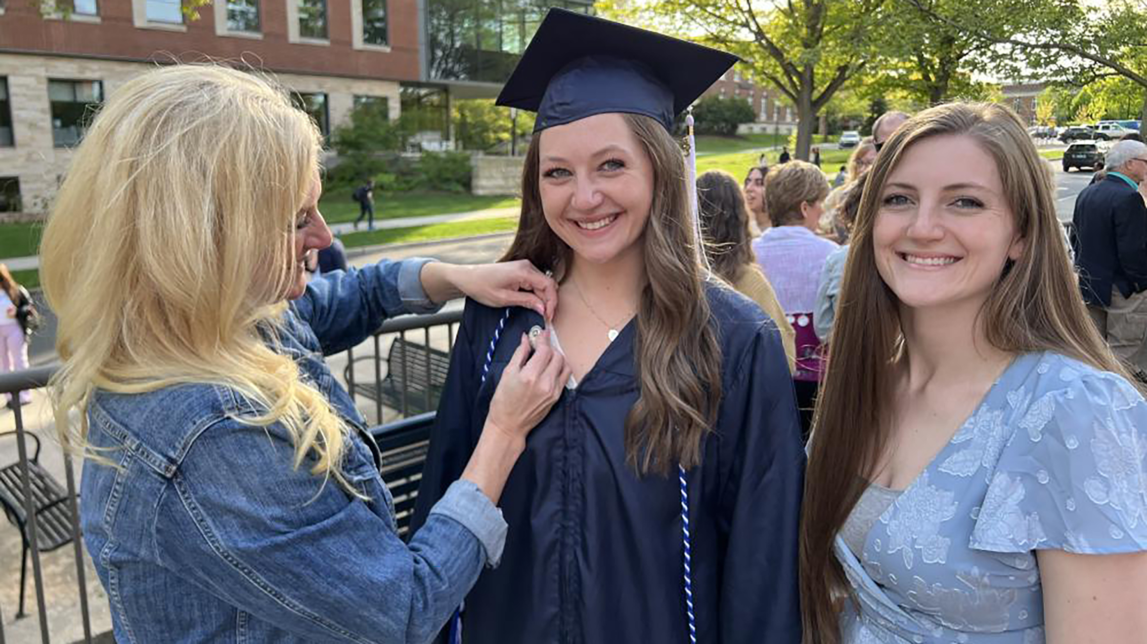 Two women pose for a photo while a third places a pin on one's shirt.