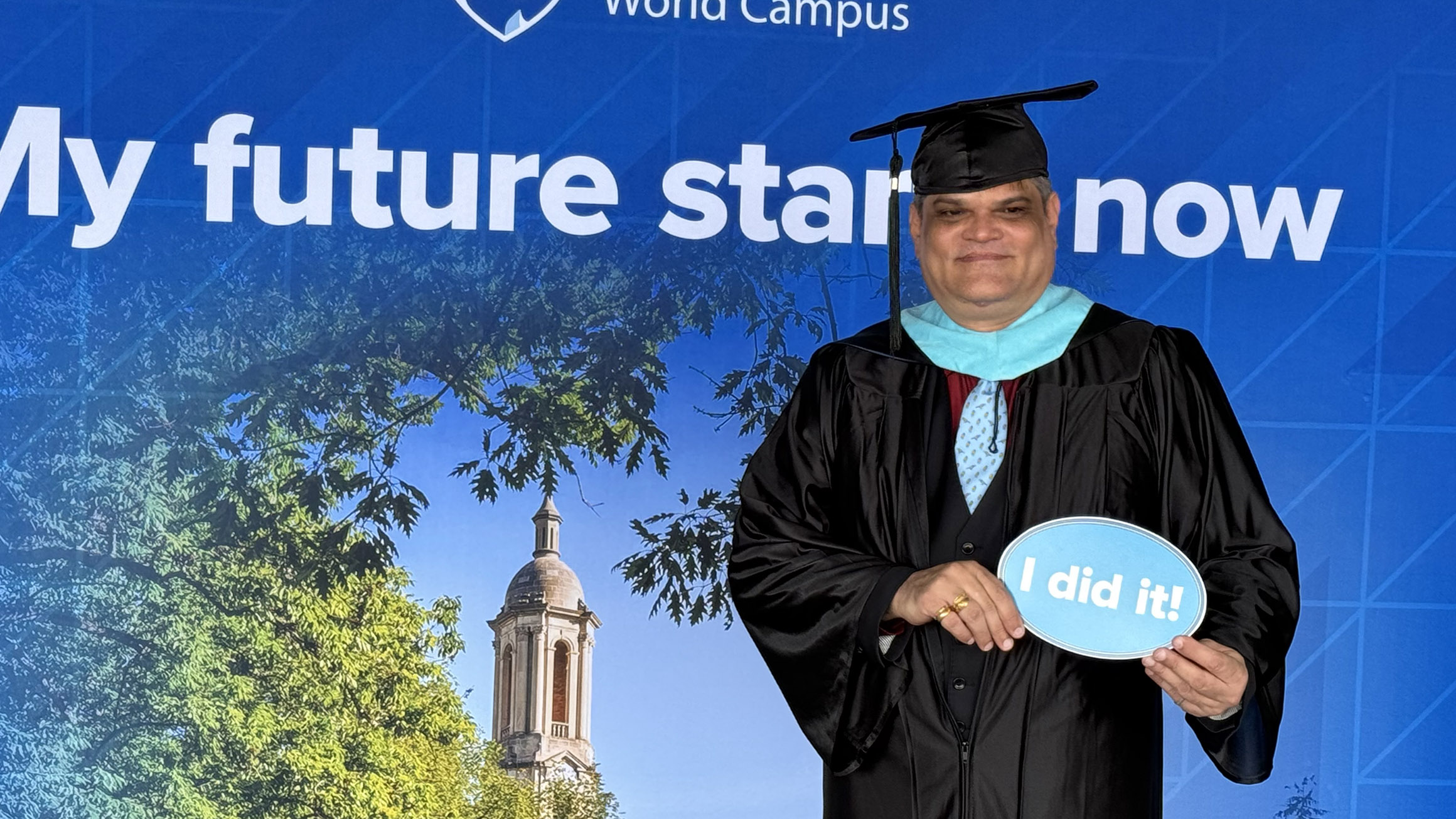 A man holding a sign "I did it!" in a graduation cap and gown