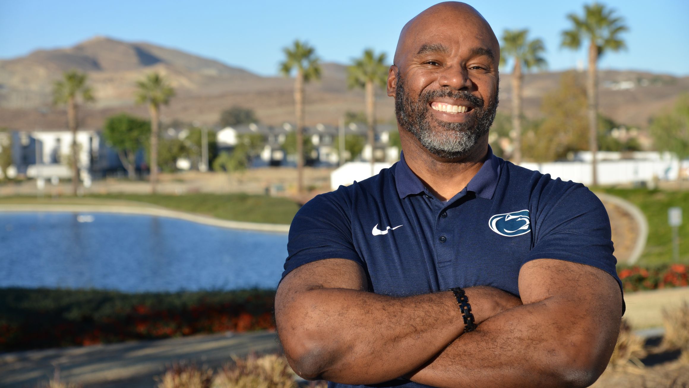 Corey Wheeler stands with his arms crossed with a pond and palm trees in the background n