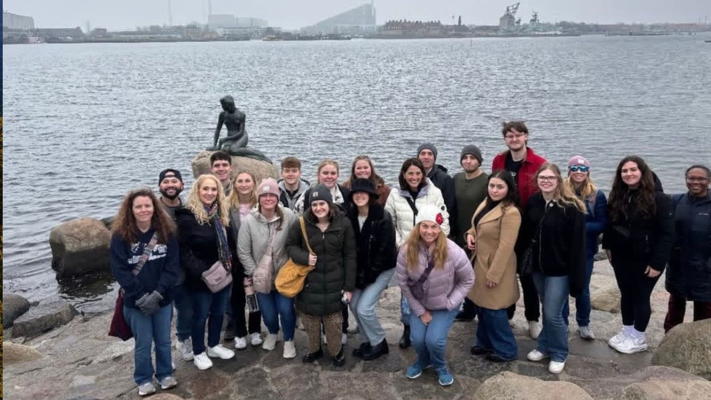 A group of people pose for a photo in front of a statue of the little mermaid