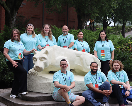 A group of people in light blue T-shirts pose for a photo around a Lion Shrine.