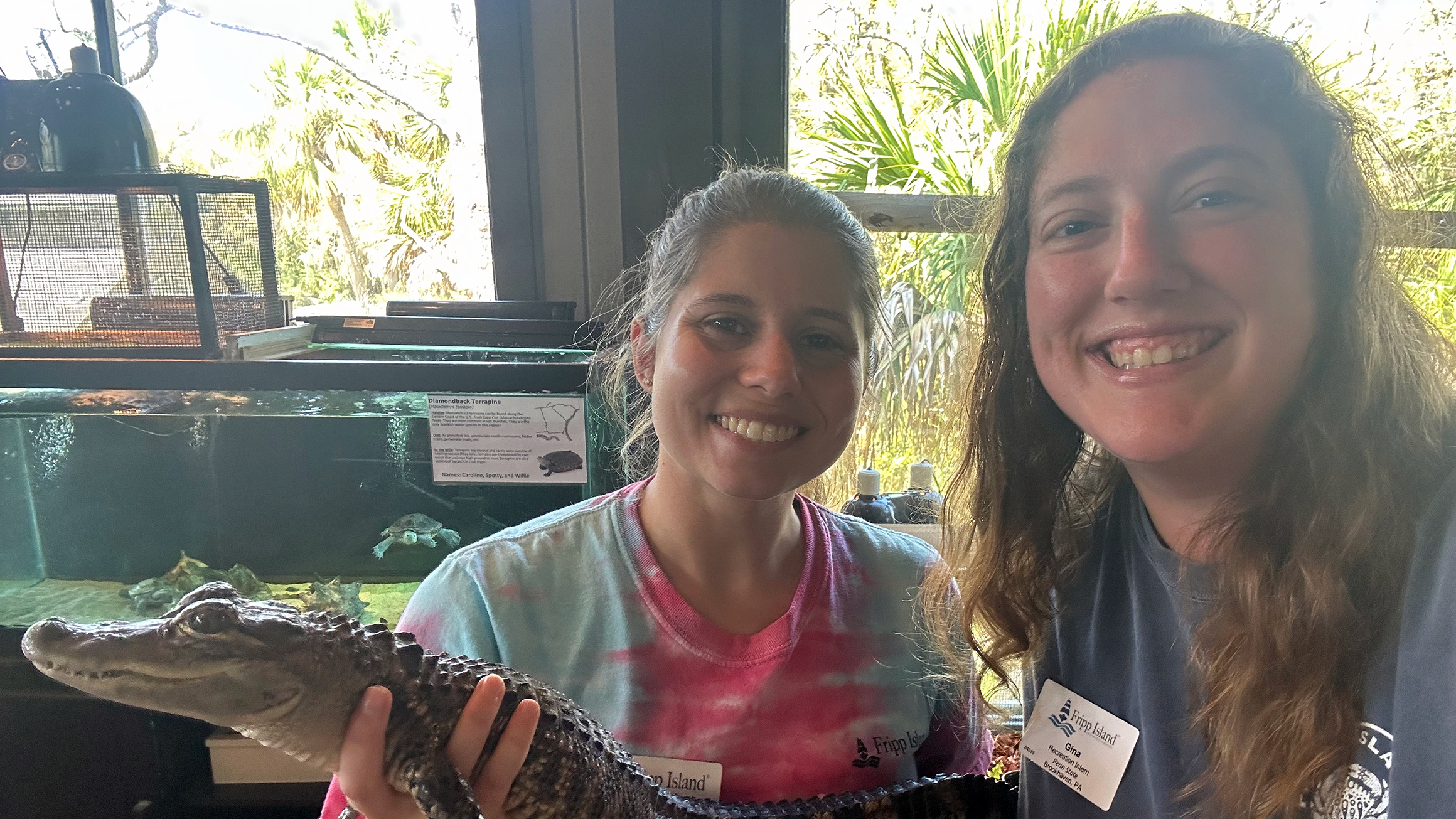 Two women pose with a small alligator.