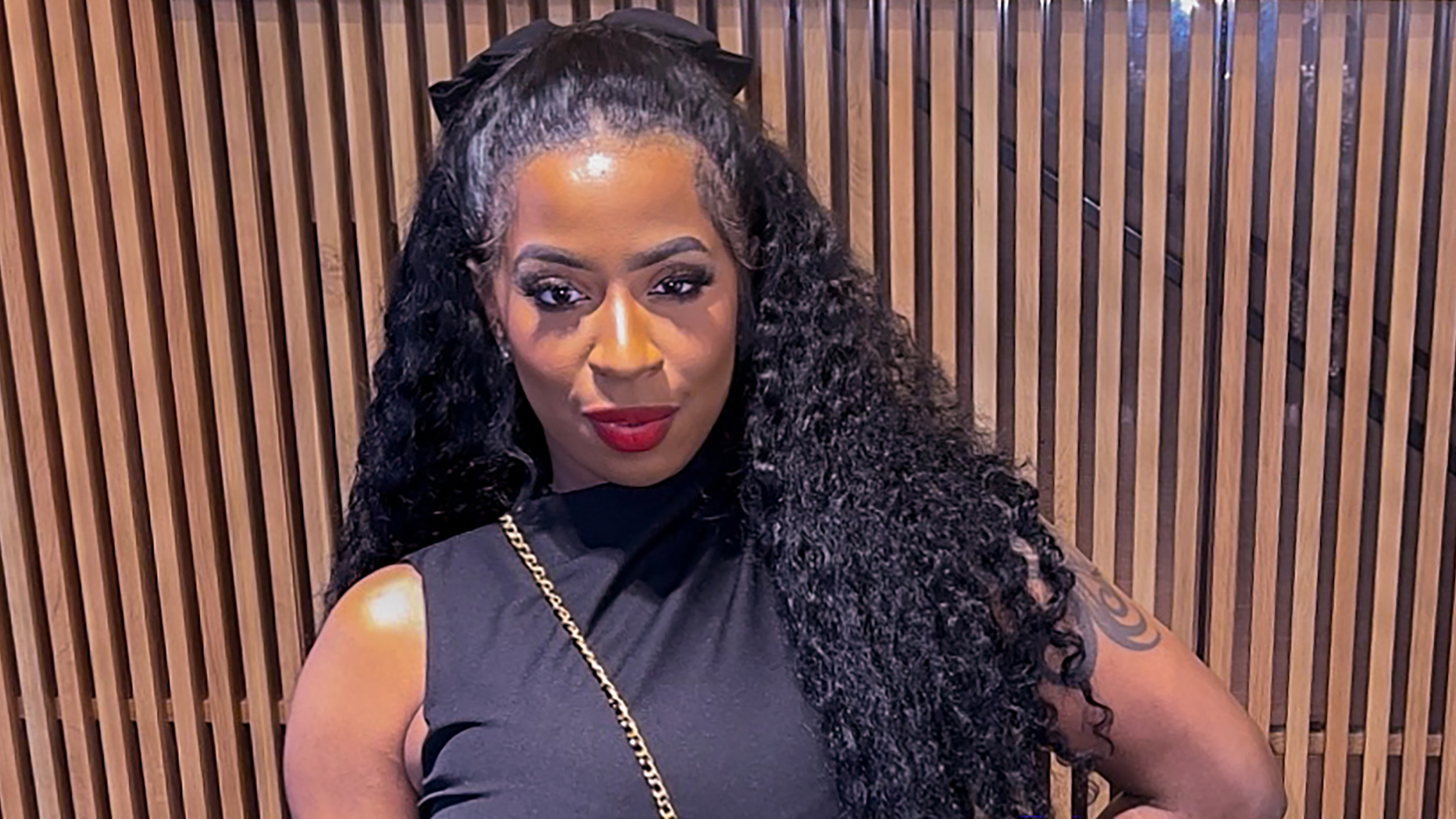 A woman wearing a black shirt in front of a textured wall.
