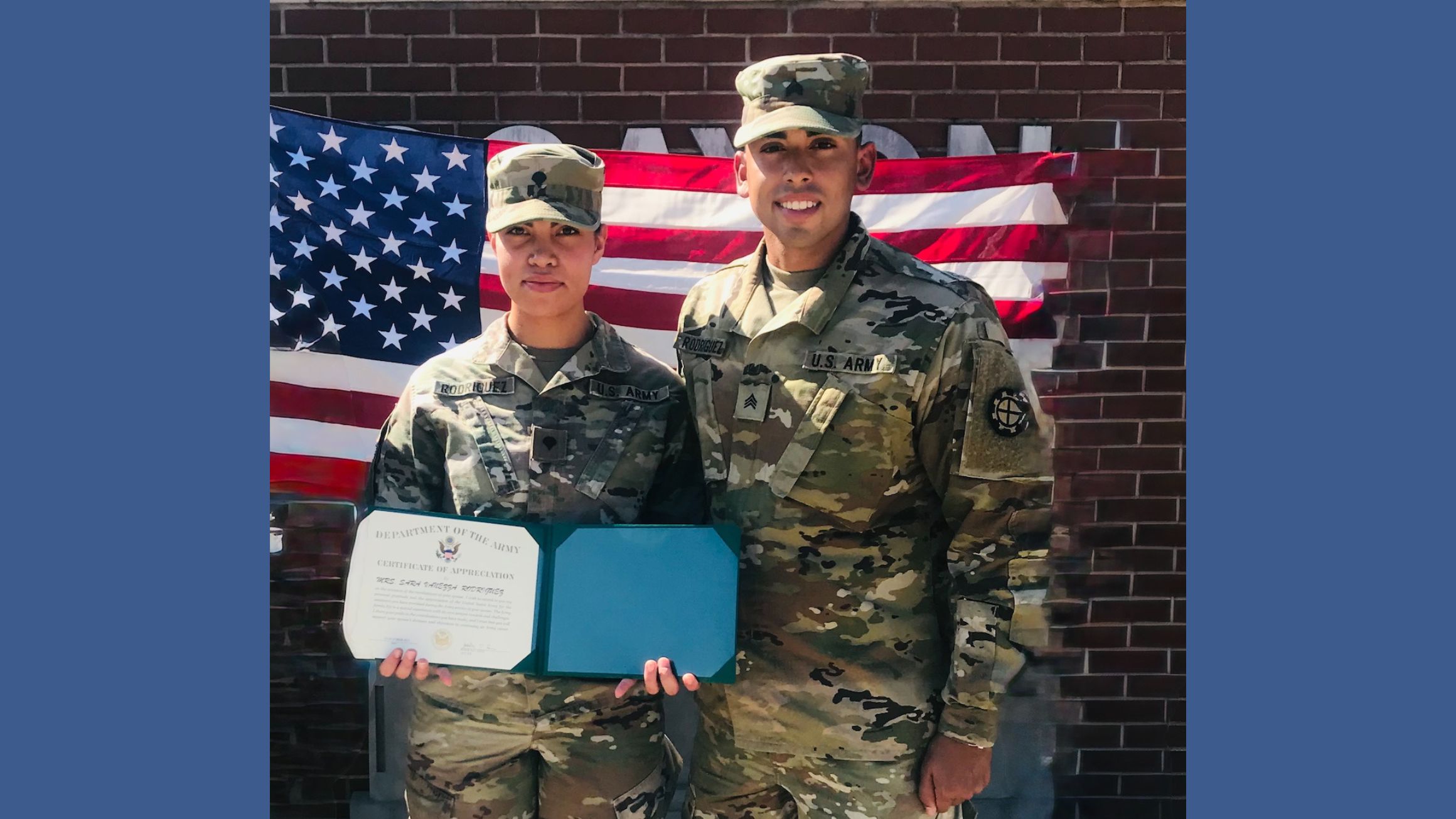 a woman and man in army fatigues post in front of a flag. the woman is holding a certificate of appreciation from the army.