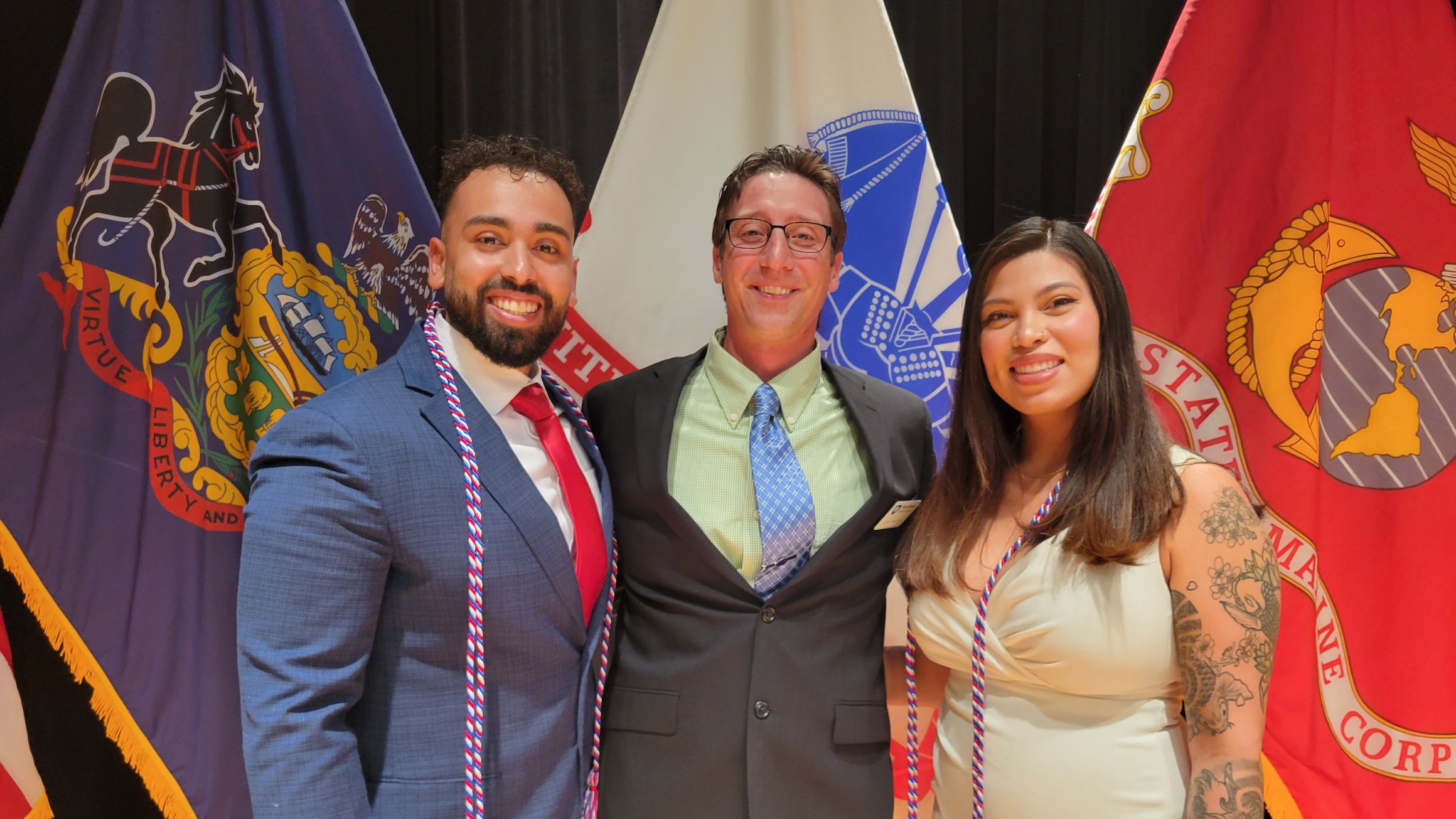 the rodriguezes pose for photo in front of military flags with their academic adviser in the middle