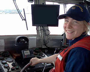A woman wearing a red life jacket driving a boat.
