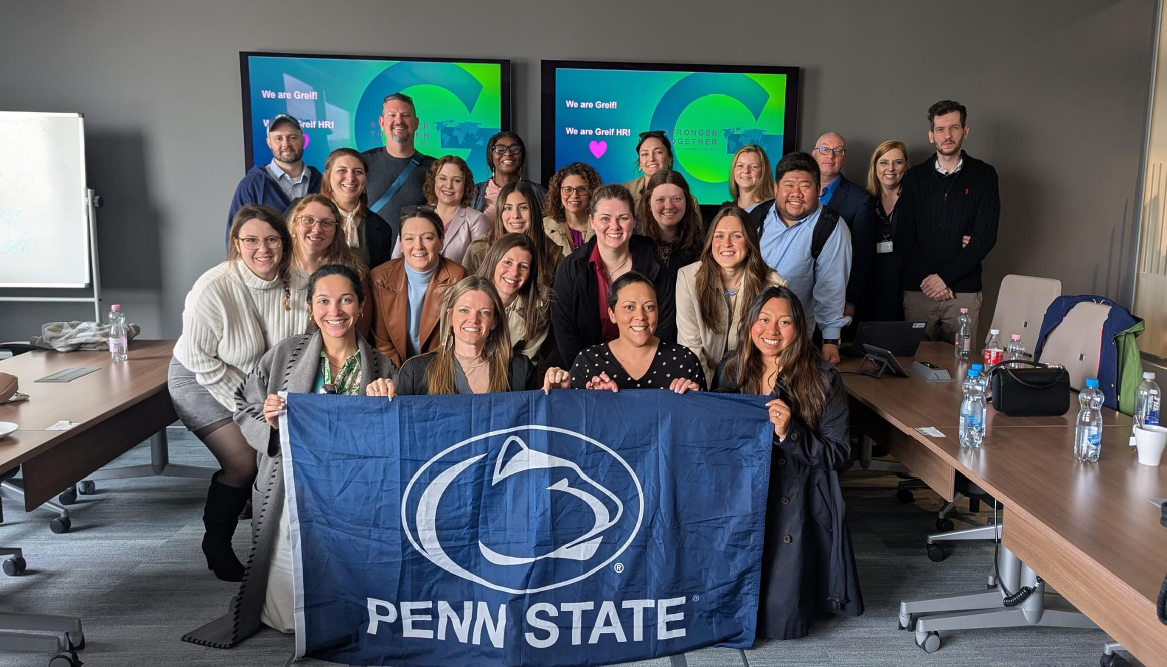 A group of people pose in a conference room with a Penn State flag.
