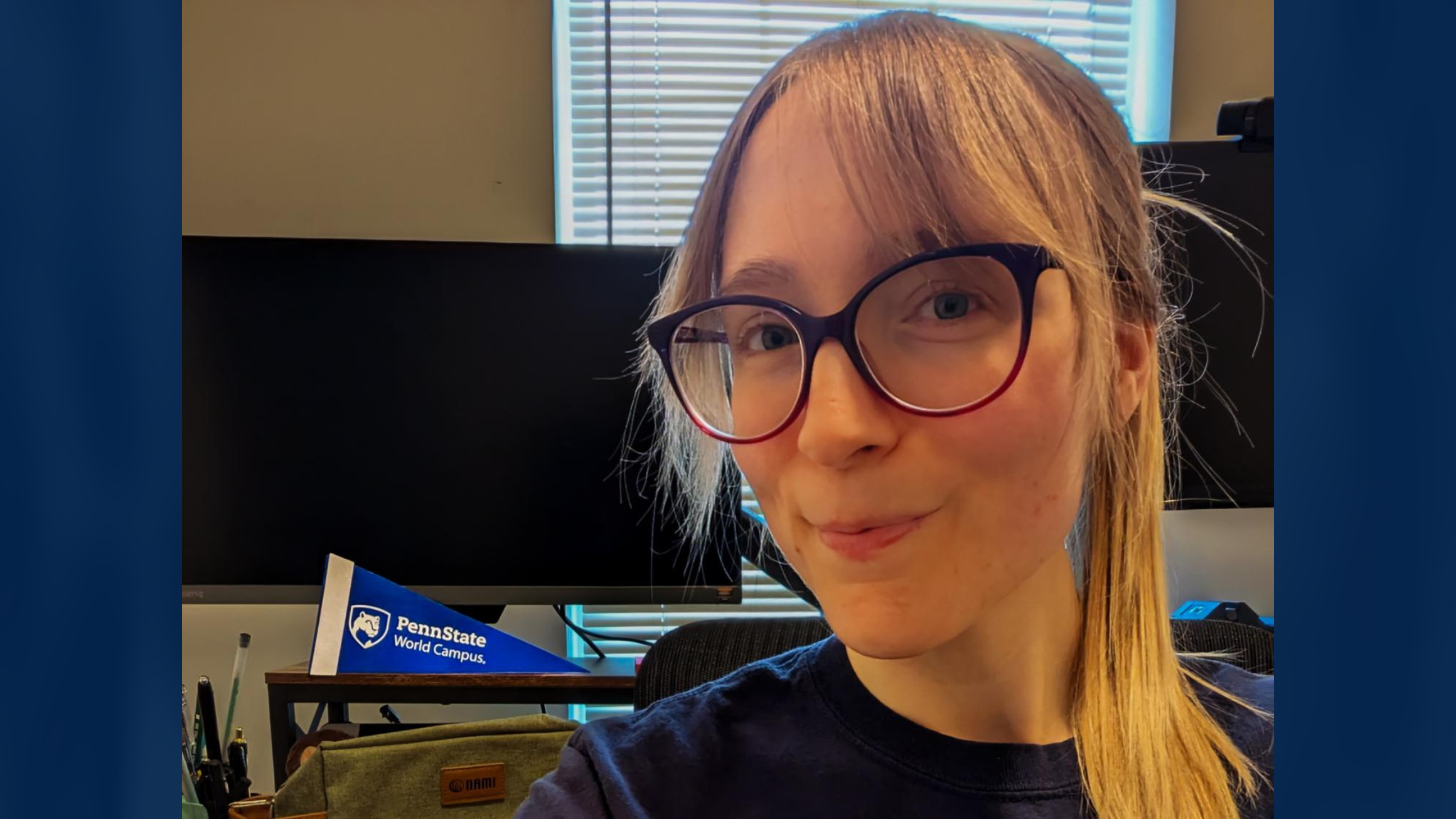A woman in front of a computer monitor with a blue Penn State World Campus pennant.