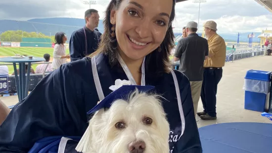 Graduate Julia Vai is wearing a blue cap and gown and her dog Riley is wearing a gap and gown that Julia designed.