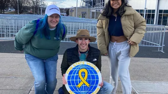 Three members of the World for THON student group post for a photo on a sidewalk outside the Bryce Jordan Center for THON 2022.