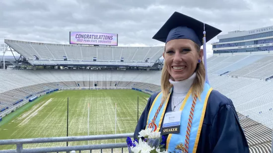 Bonnie Lim, wearing a blue cap and gown, stands with the field and bleachers of Beaver Stadium in the background