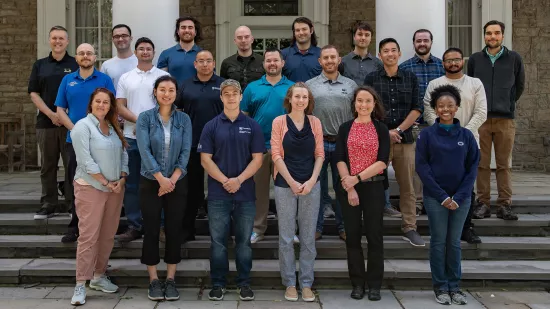 A group of students, faculty, and staff stands in front of the Hintz Family Alumni Center.