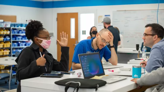 Three people sit at a lab desk collaborating on a project.