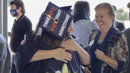 Two graduates hug one another as another person looks on.