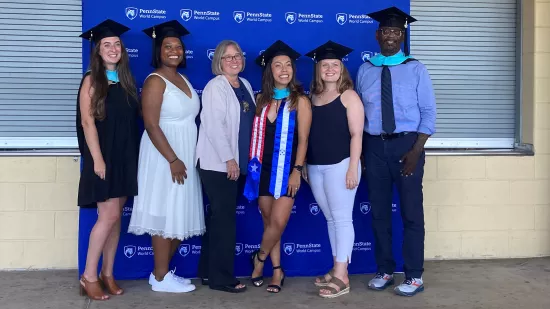 Six people pose for a photo in front of a blue Penn State backdrop.