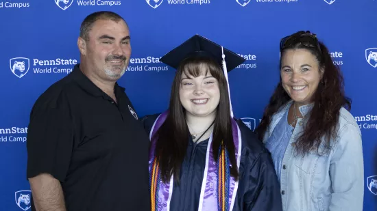A graduate poses with her parents in front of a blue background.