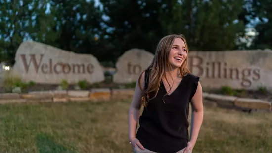 Photo from Maddie Reiners Photography Mallerie Stromswold stands in front of a sign on rocks that reads "Welcome to Billings"