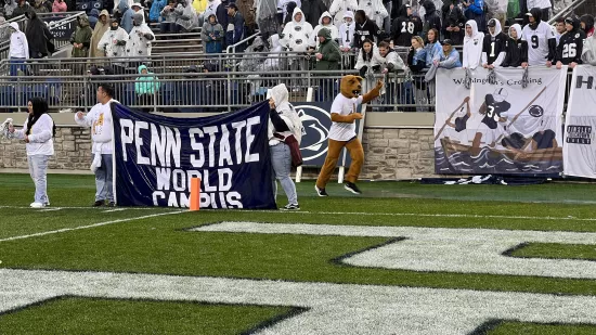 The Nittany Lion runs by the Penn State World Campus students holding the banner.