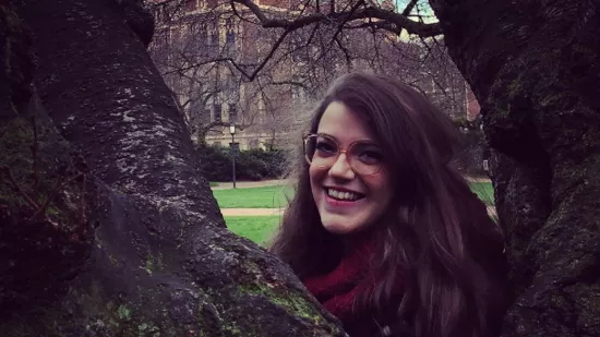 Michelle Funk poses for a photo between two branches of a tree with a classroom building in the background