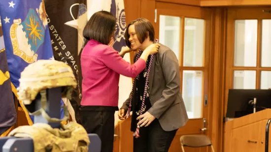 A woman places a honor cord on the shoulders of another woman.