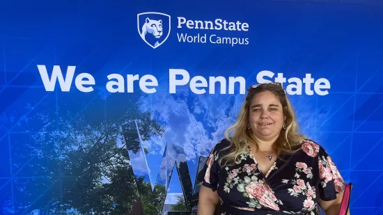 Kim Reiker stands in front of a backdrop that shows the Penn State World Campus logo and the text "We are Penn State"