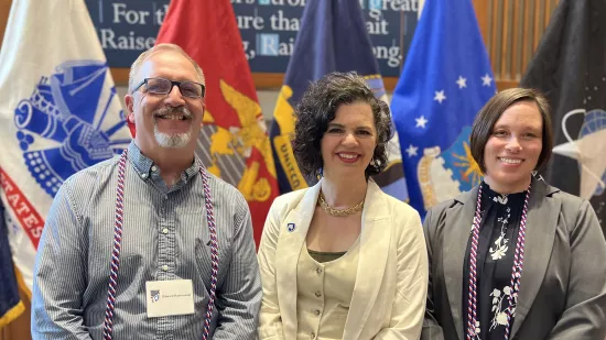 Edward Rusinowski, Rose Petrunyak, and Jenny Brunson stand in front of flags on a stage