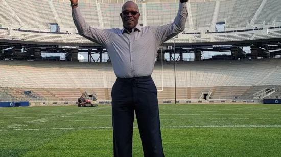 Brian K. White makes the hand motion signaling a touchdown standing on the field at Beaver Stadium with the stands in the background.