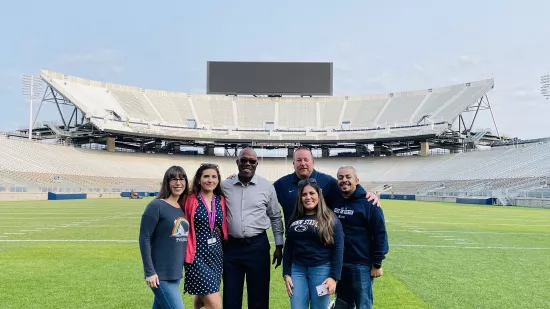 Six students stand on the field with the stands of Beaver Stadium in the background