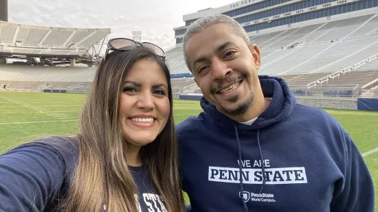 Jackie Salan and Saleh Maghrabi take a selfie on the field of Beaver Stadium with the stands behind them in the background.