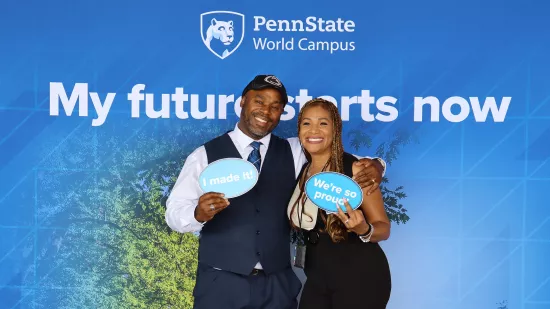 A man and woman stand together in front of a Penn State–themed backdrop.