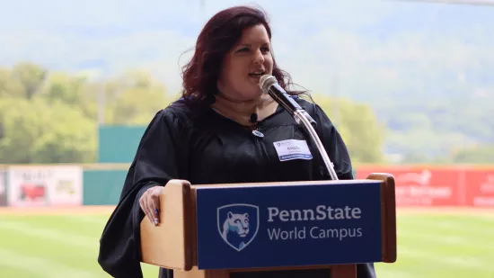 A woman wearing a black graduation cap and gown speaks at a podium.