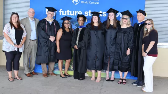 A group of people stand in graduation regalia in front of a blue and white background.