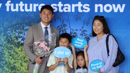 A man, woman, and two children hold signs in front of a Penn State–themed backdrop.