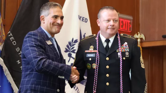 A man in a suit shakes the hand of a man in a dress military uniform