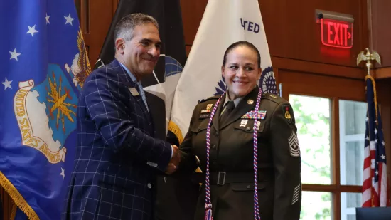 A man in a suit shakes hands with a woman in a military uniform