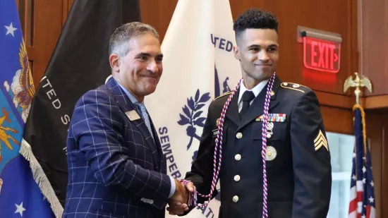 A man wearing a suit shakes the hand of a man wearing a dress military uniform.