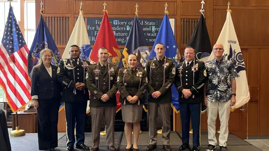 A woman and men in military uniforms stand on a stage