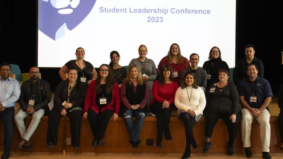 A group of people pose on a stage in front of a presentation screen.