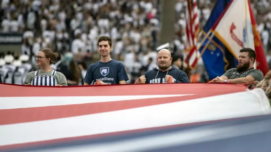 A group of people hold onto a large American flag.