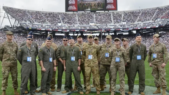 Military men wearing camouflage and green uniforms stand in a line on the field of Beaver Stadium