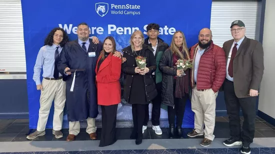 A group of people pose in front of a Penn State background.