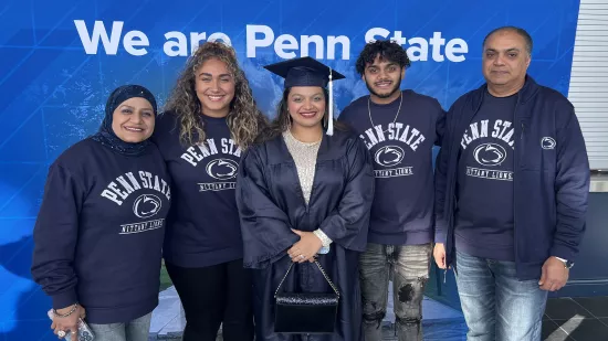 A Penn State graduate in a cap and gown stands with four members of her family, who all wear sweatshirts that say "Penn State Nittany Lions."