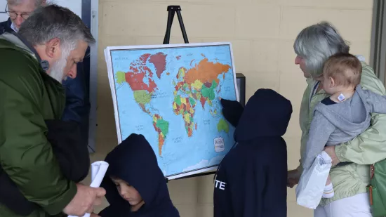 Two adults and three children looking at a world map.
