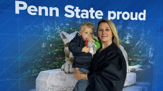 A woman in a graduation gown holding a toddler.