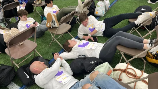 Three people lay on the ground with their legs resting on chairs.